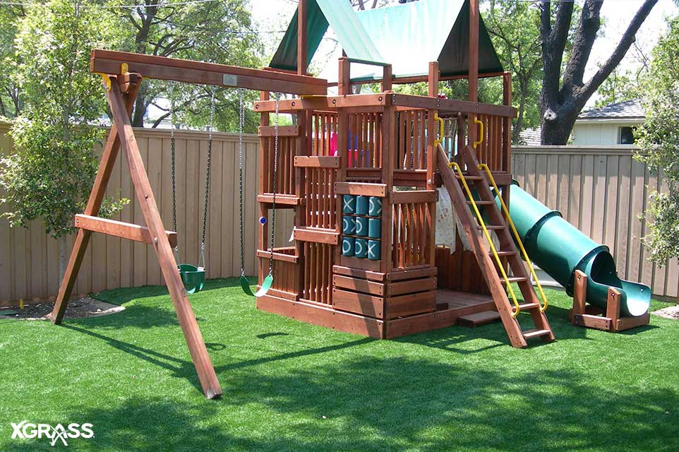 Backyard playground made out of wood with synthetic grass around it